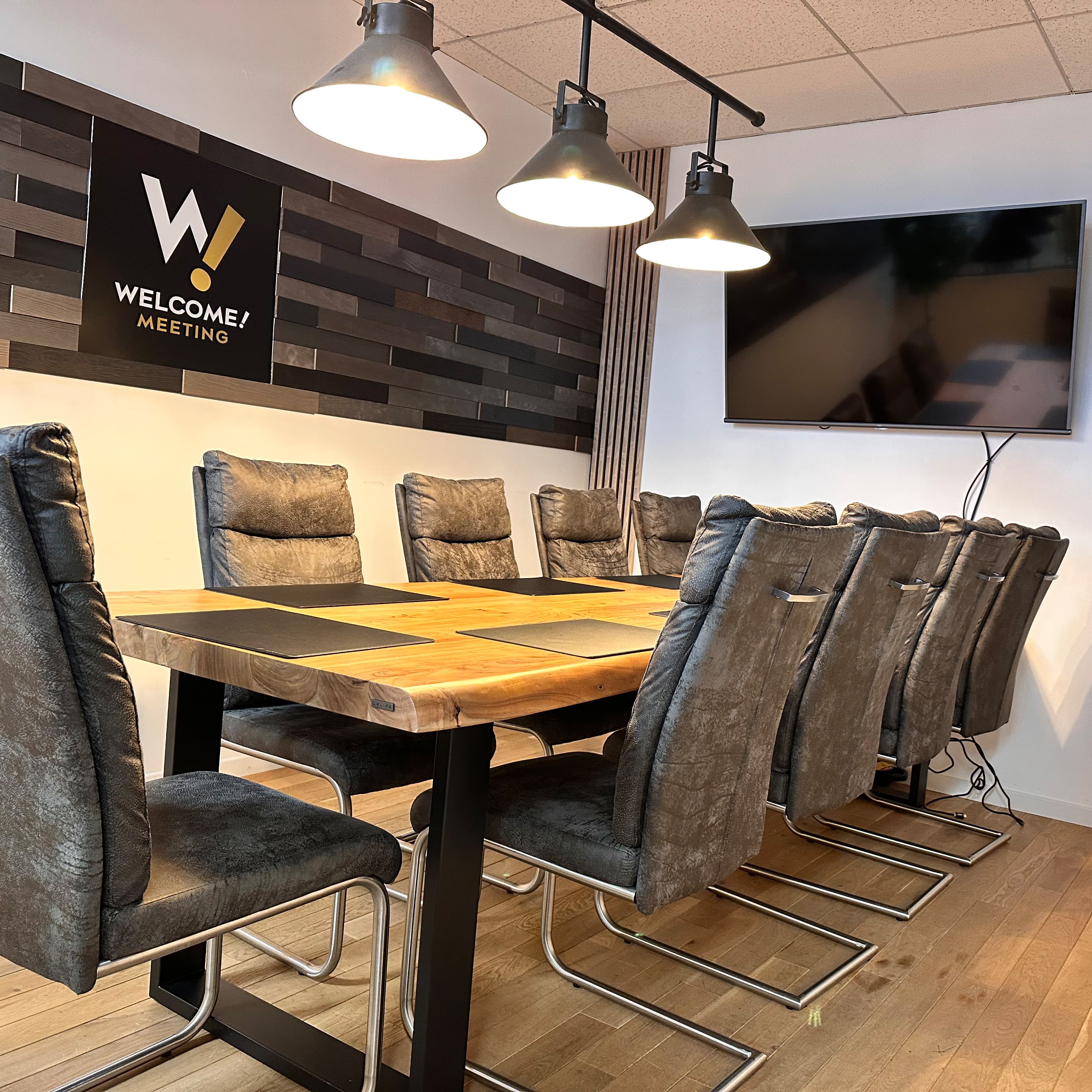 Welcome-Besprechungsraum mit Holztisch, Sesseln und großem Bildschirm